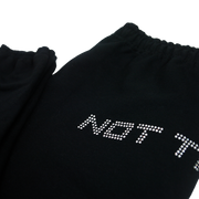 Close up of top of black sweatpants lying flat, text visible is "Not T" in silver rhinestones.