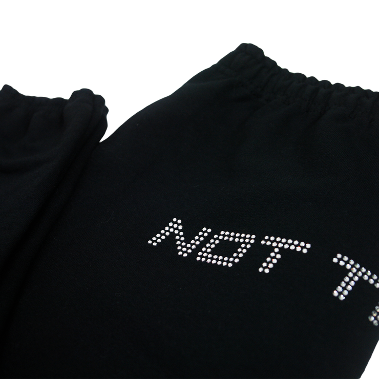 Close up of top of black sweatpants lying flat, text visible is "Not T" in silver rhinestones.