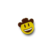 Photo of a enamel pin with yellow, brown and white smiley face with a cowboy hat.  silver sides can be seen.  On a white background.